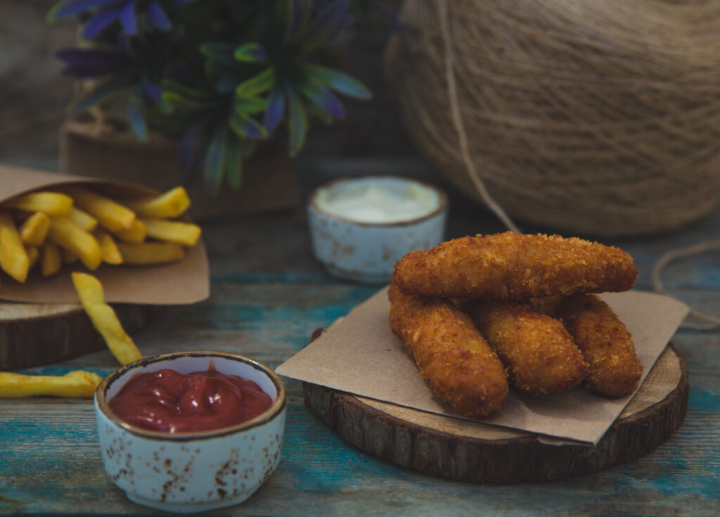 Crispy fish fingers cooked in an air fryer, served with ketchup, fries, and a creamy dipping sauce on a rustic wooden surface.