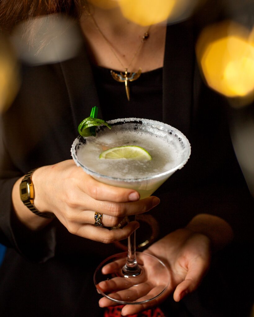 A person holding a festive Christmas cocktail with a salted rim and a lime wedge garnish, perfect for the holiday season.